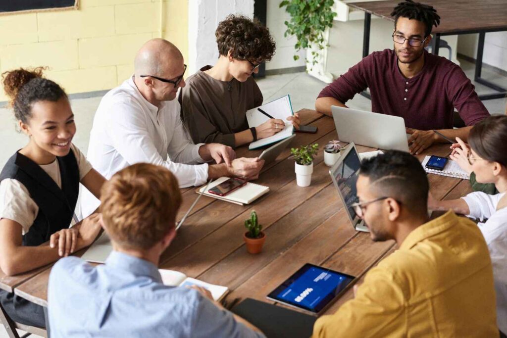 Diverse group of people collaborating around a wooden table with laptops and notebooks