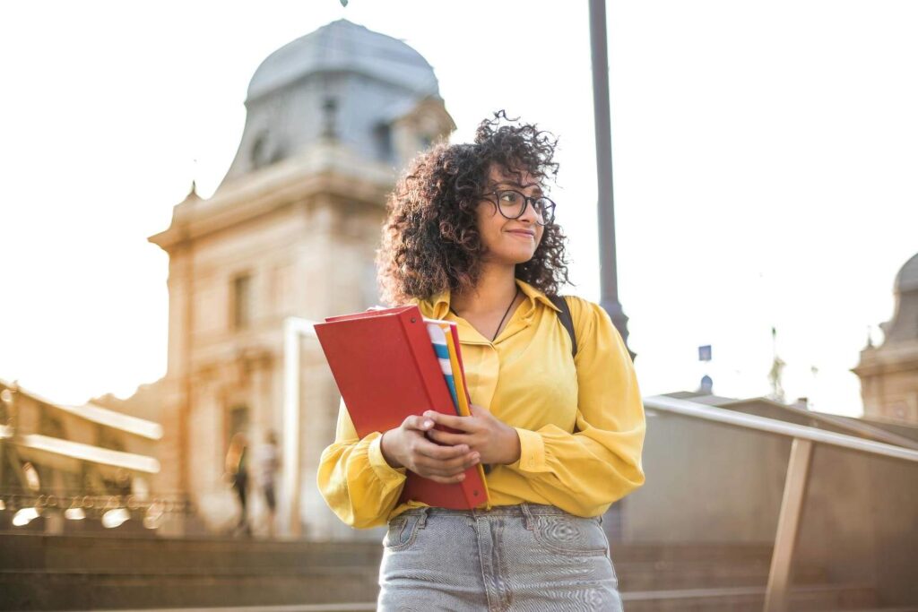 Smiling student holding folders while standing outdoors