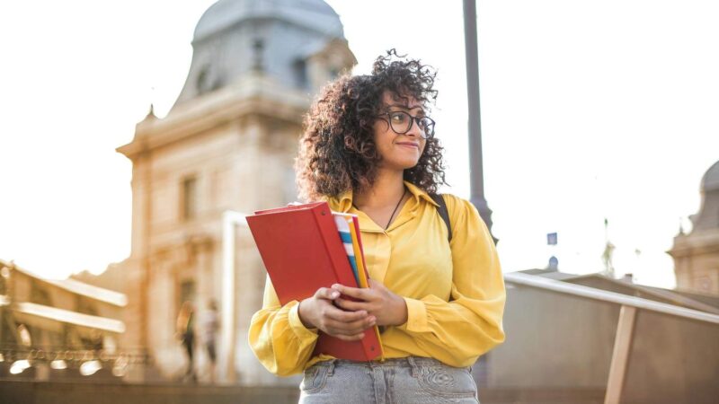 Smiling student holding folders while standing outdoors
