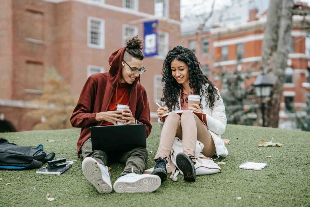 students on the grass with laptop and notebooks