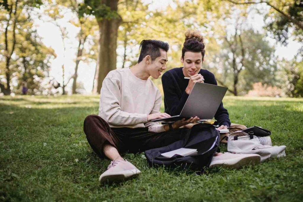 Two students sitting on the grass with a laptop, studying together