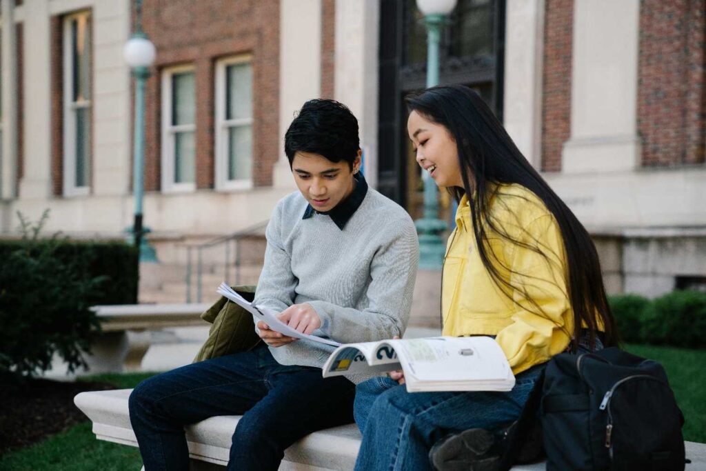 Two college students studying together with books on a campus bench