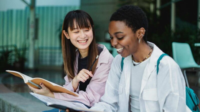 Two students sitting and happily discussing about their notes