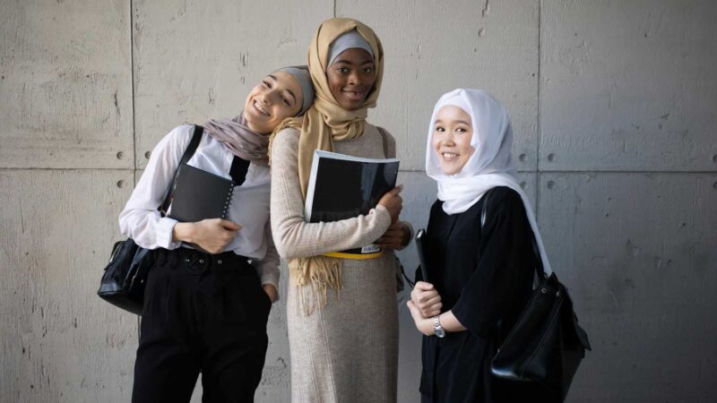 Three diverse students with hijab carrying notebooks