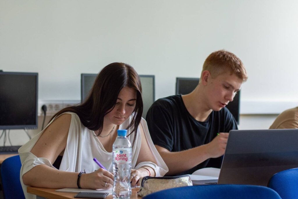 alt text: Two students focused on studying using a laptop and taking notes