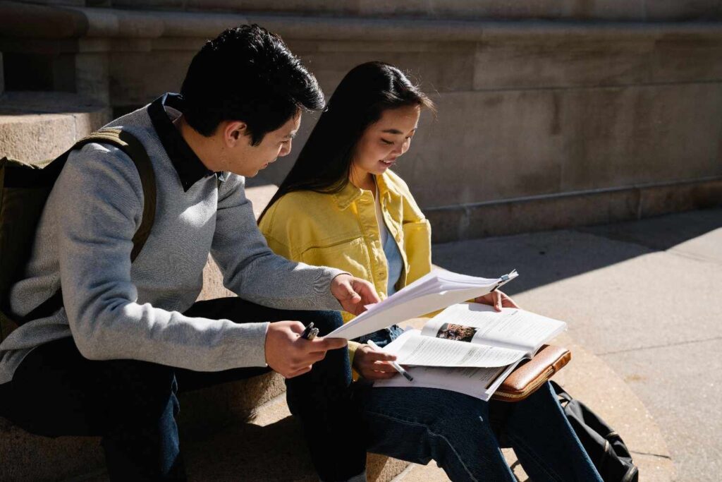 Two students study together outside, engaging in reading and discussion